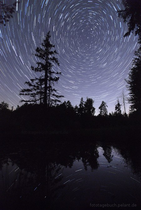 Sternspuren (Startrails) spiegeln sich im Birkensee bei Nacht. Im Zentrum der Rotation ist der Polarstern.