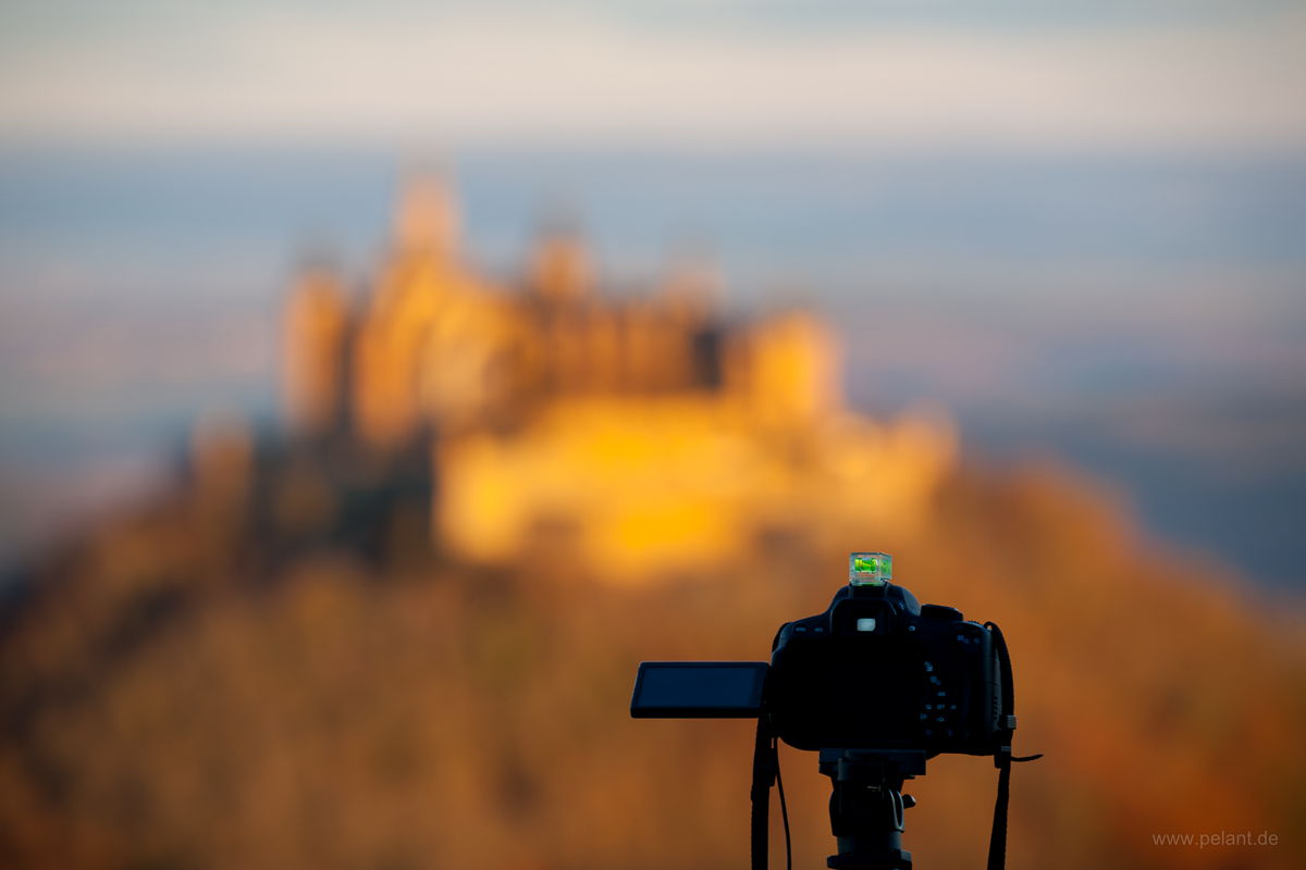 Kamera auf einem Stativ, dahinter (unscharf) die Burg Hohenzollern im Morgenlicht